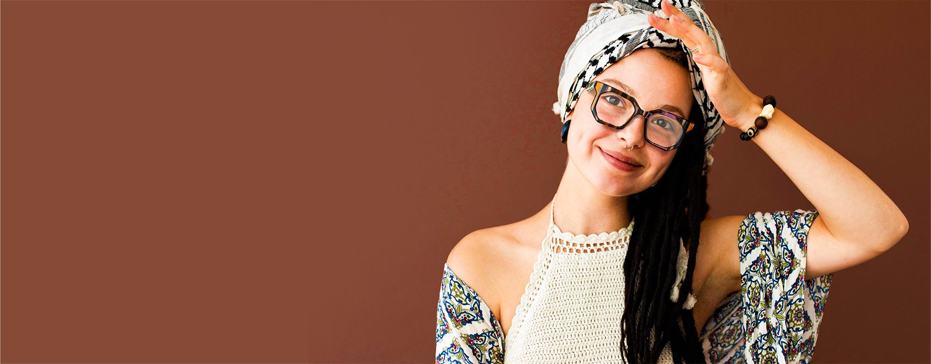 Bohemian style model adorned with flowers and bohemianism frame glasses, set against a vibrant textile background.