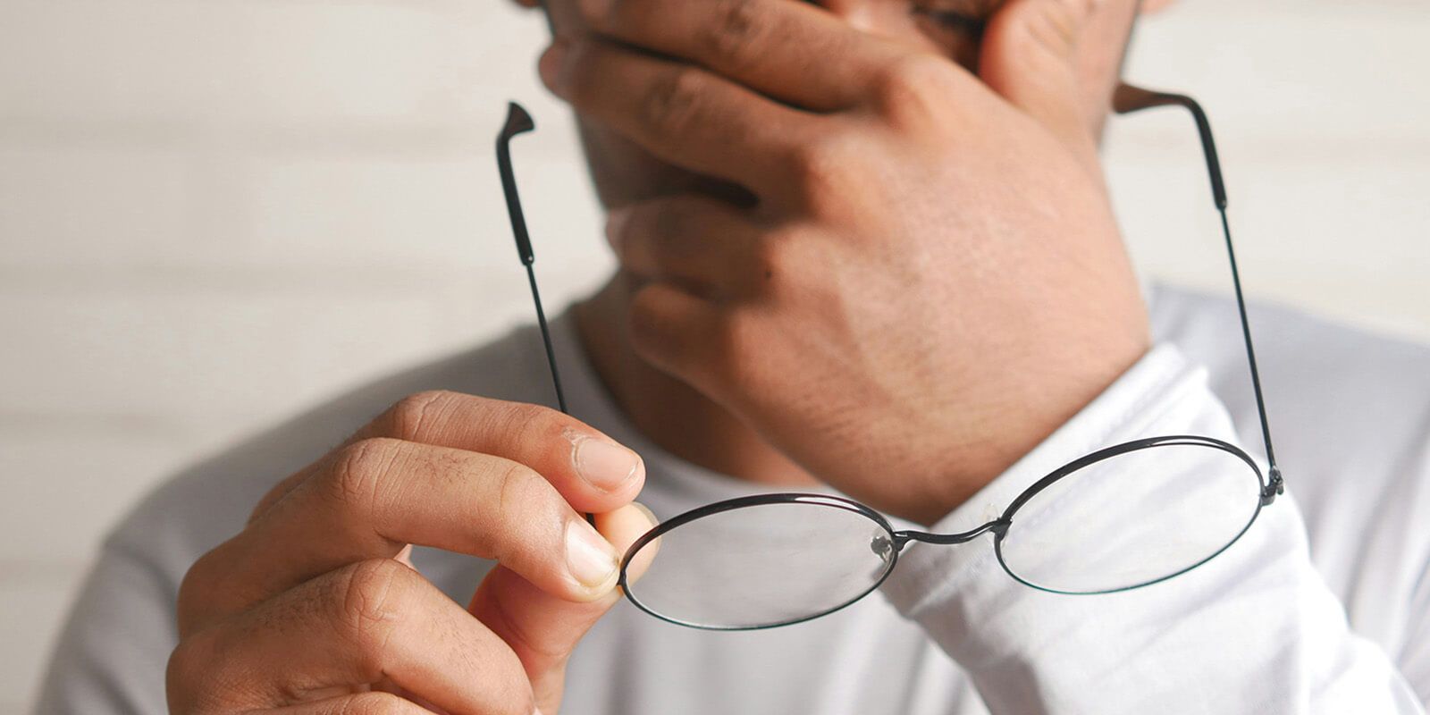 A man, is holding a pair of round eyeglasses, one hand near the bridge of the glasses and the other supporting the temple