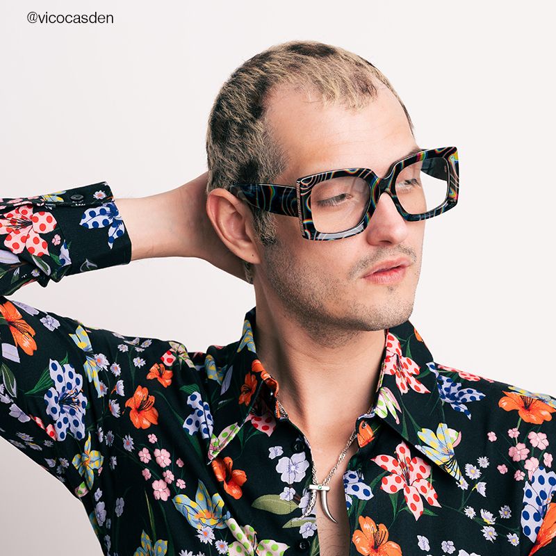 A man wearing colorful, patterned glasses and a black, floral shirt.