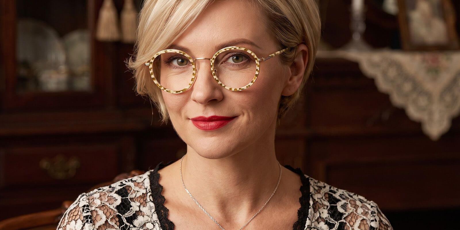 A woman's smiling face with bright green eyeshadow and try on round glasses with silver detailing.