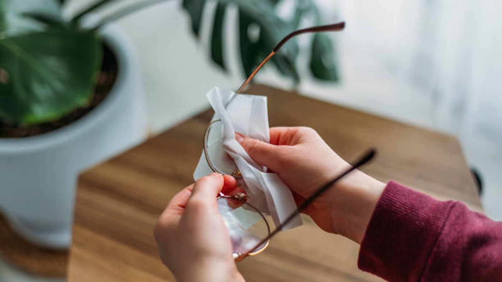 A close-up of hands holding a pair of glasses while wiping the lenses with a cleaning cloth.