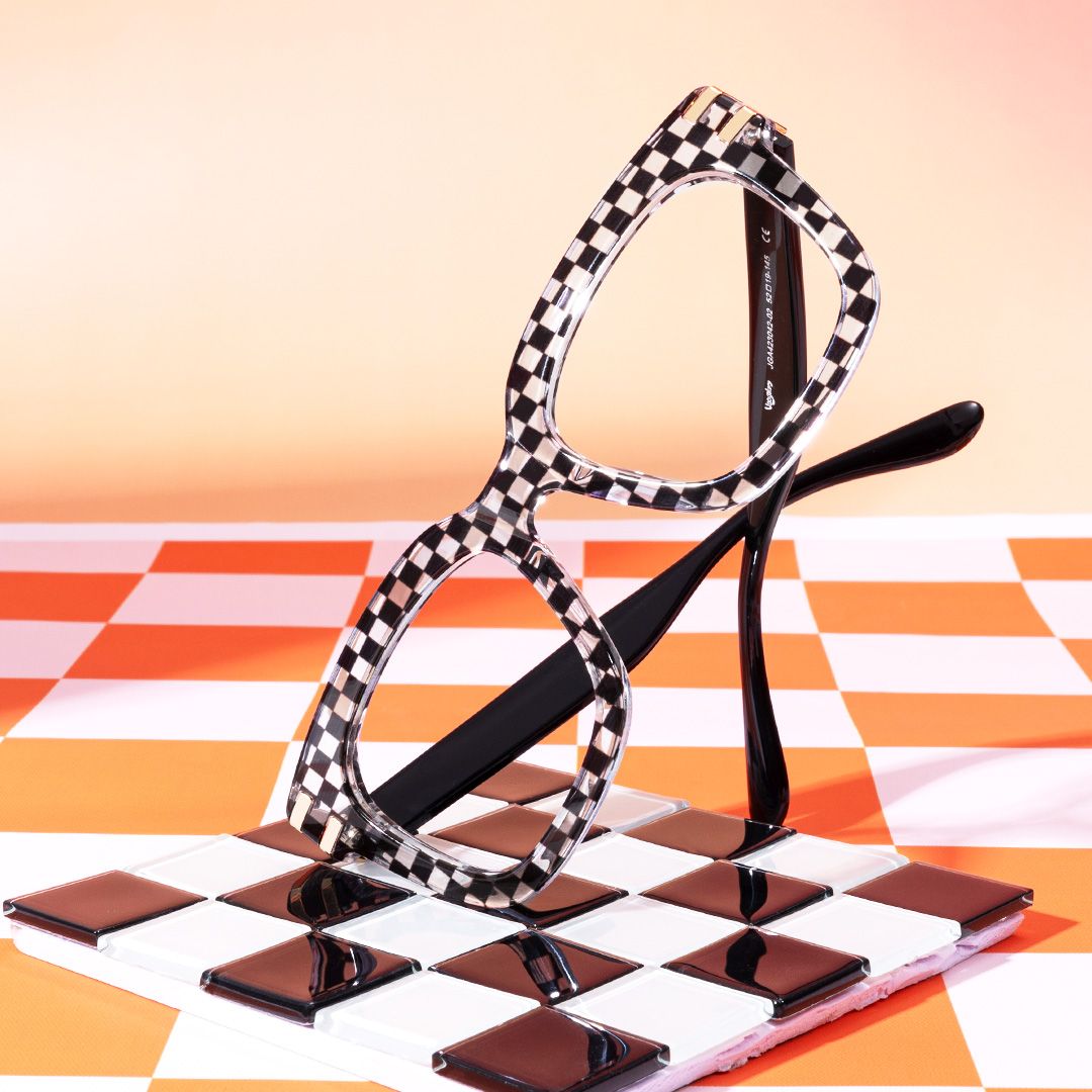 A pair of black and white checkered glasses stands upright on a checkerboard surface with an orange and white checkered background.