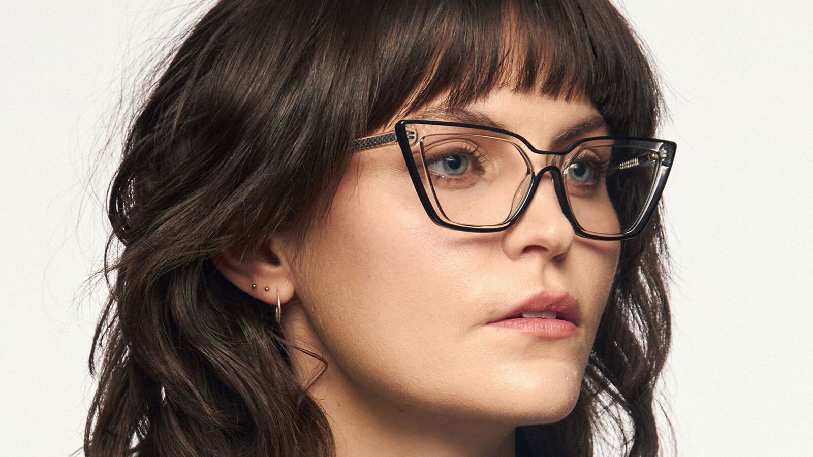 A woman with wavy brown hair and bangs wears a pair of black cat-eye glasses with clear lenses